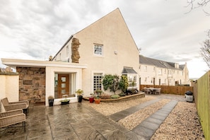 Ein modernes Haus mit Naturstein-Fassade, einer Terrasse mit Gartenmöbeln und einem Gartenbereich.
