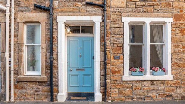 Un edificio de piedra con una puerta azul, una ventana con flores y un letrero que dice 'Nolish Cottage'.