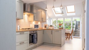 Una cocina moderna con armarios grises, microondas y estufa. Hay luces colgantes y un tragaluz sobre la encimera.