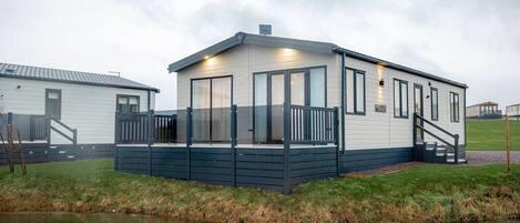 A single-story mobile home with a covered porch, a small staircase, and a grassy area in front.