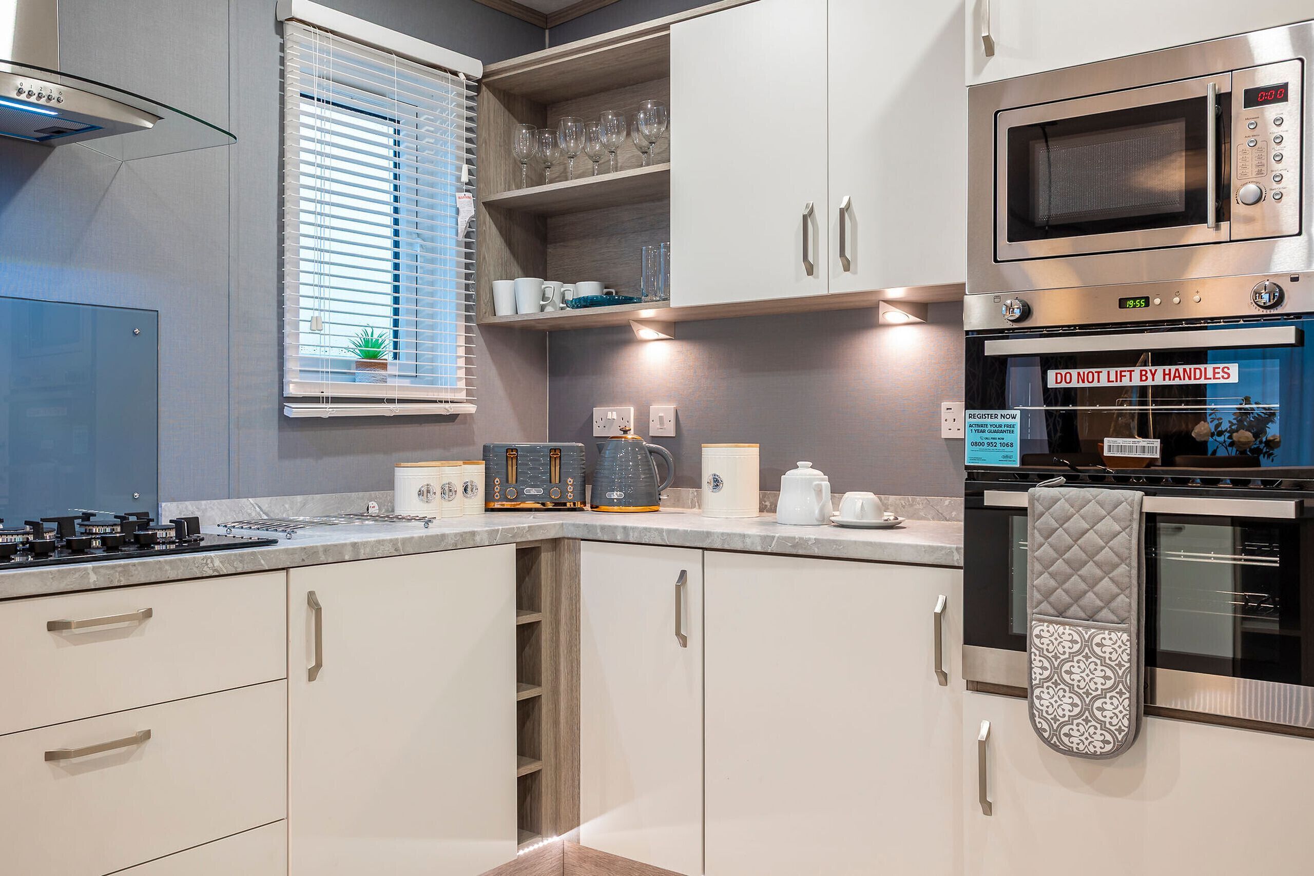 Una cocina moderna con armarios blancos, horno empotrado, microondas y una ventana con persianas.