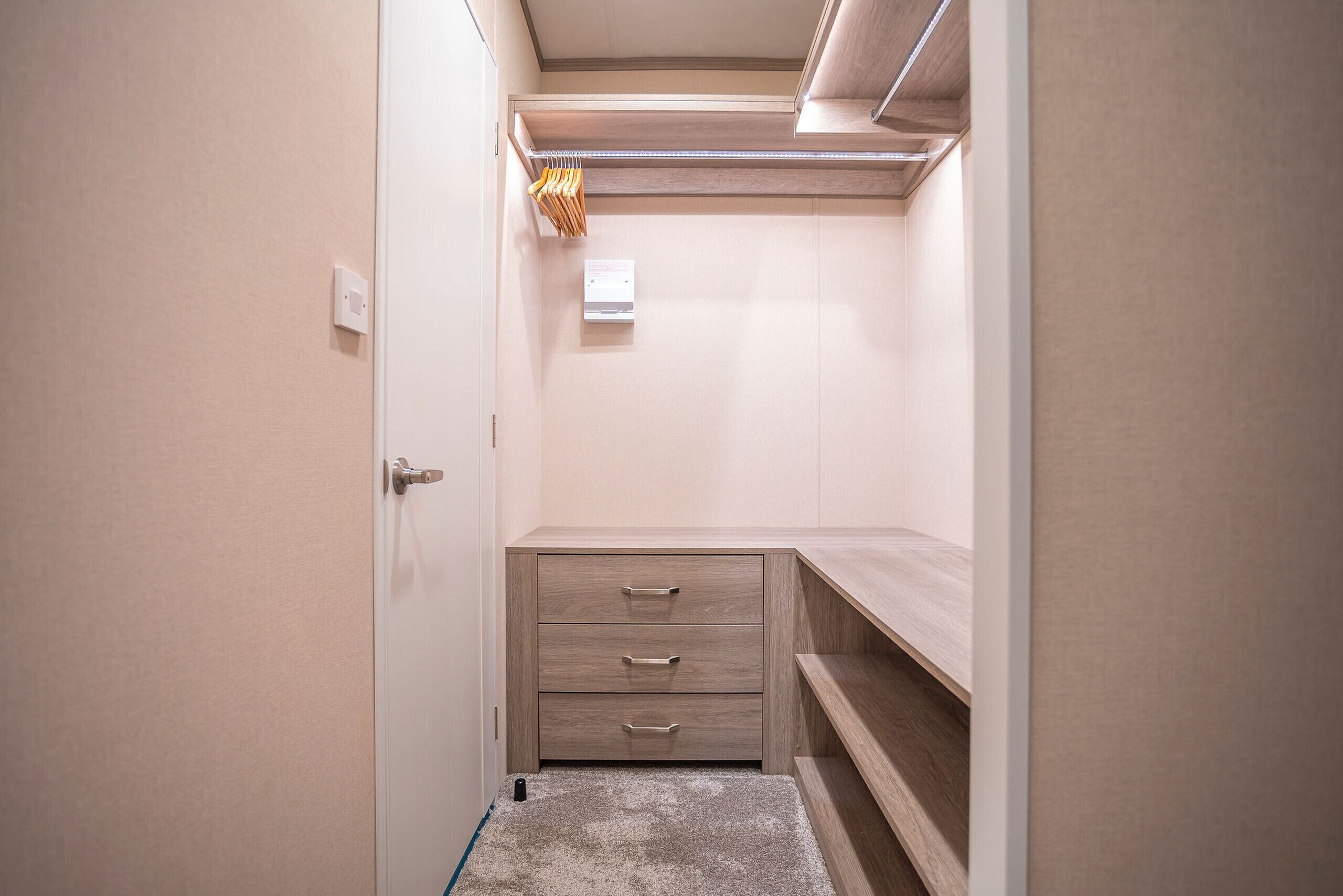 Un petit dressing avec une étagère en bois, une tringle à vêtements et un meuble à tiroirs intégré.