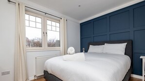 Ett sovrum med en stor säng, ett fönster med gardiner, ett element och en blå väggpanel.