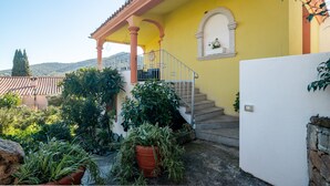 Un edificio giallo con una scala che conduce a un balcone, circondato da piante in vaso e un muro di pietra.