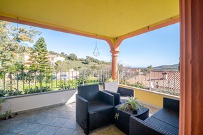 A covered balcony with wicker furniture, a hanging light fixture, and a view of a hillside. - Holiday Home 'La Casa di Piera 1' with Sea View, Wi-Fi and Air Conditioning (San Pietro)