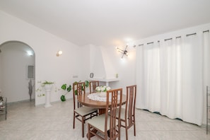 Un coin repas avec une table ronde en bois, six chaises, une plante en pot et un mur blanc agrémenté d’un luminaire.