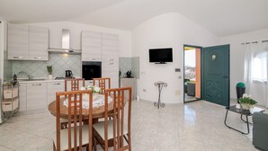 Una cucina compatta con elettrodomestici moderni, un'area pranzo con tavolo e sedie in legno, e una porta verde che dà sull'esterno.
