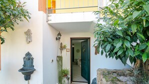 Une entrée étroite, avec un mur en pierre, une fontaine en métal et des plantes en pot.