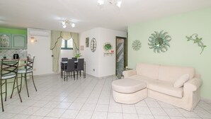 Un salon avec un canapé, un coin repas avec des chaises et une cuisine équipée d’un réfrigérateur.