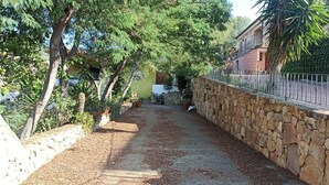 Un sentier étroit, bordé de murs de pierre et d’arbres, mène à un bâtiment à la façade jaune.