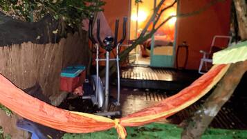 Un hamac est suspendu entre deux arbres dans un coin du jardin, à proximité d’une chaise et d’une table en métal.
