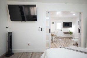 Ein Hotelzimmer mit einem Bett, einem an der Wand montierten Flachbildfernseher, einem Standheizgerät und einer Tür zu einem Essbereich mit Tisch und Stühlen.