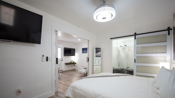 Et moderne soveværelse med en stor seng, et fjernsyn monteret på væggen og et walk-in closet med hylder.