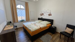 A bedroom with a bed, bedside tables, a desk, a chair, a window with curtains, and a wall decal.