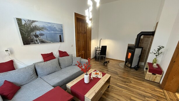 A modern living room with a grey sofa, red cushions, a wooden coffee table, a fireplace, and a painting of a coastal scene.