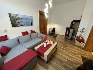 A modern living room with a grey sofa, red cushions, a wooden coffee table, a fireplace, and a painting of a coastal scene. - Apartment 'Haus Silky' with Private Pool, Garden, and EV Charging Station (Weida)