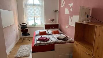 Een slaapkamer met een bed, een bureau, een stoel, een kledingkast, een raam met gordijnen en een plafondlamp.