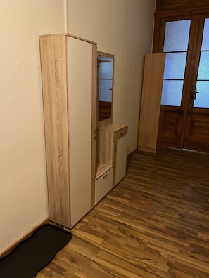 A room with a wooden wardrobe, a small cabinet, a black mat on the floor, and a wooden door with frosted glass panels. - Apartment 'Haus Silky' with Private Pool, Garden, and EV Charging Station (Weida)