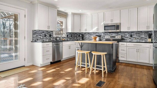 A modern kitchen with white cabinets, a black and white backsplash, and a central island with stools. - Clemens House - Relaxing Lexington Home for Long Stays (Lexington)