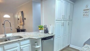 Una cocina moderna con armarios blancos, encimera de granito, pileta de acero inoxidable y lavavajillas integrado.