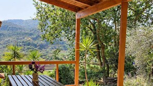 Una veranda esterna con tavolo e sedie di legno, immersa nel verde e con vista sulle colline.