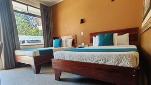 A hotel room with two wooden beds, a window with curtains, and a tiled floor. - Hotel Wilson Condega (Liberia)