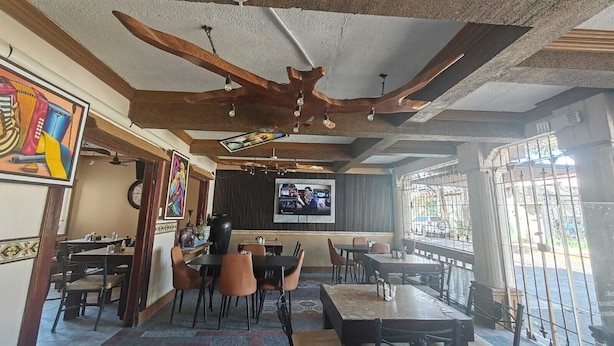 A restaurant with wooden ceiling beams, a TV screen, and tables with chairs. - Hotel Wilson Condega (Liberia)