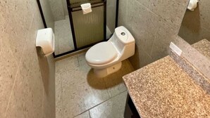 A small, tiled bathroom with a toilet, a shower enclosure, and a granite countertop. - Hotel Wilson Condega (Liberia)