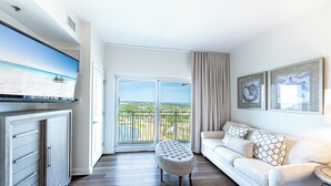 Ett modernt vardagsrum med en vit soffa, en vadderad bänk och en platt-TV placerad på ett träskåp.