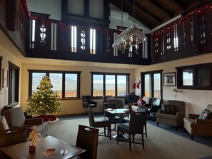 Un salon spacieux, agrémenté d’un grand sapin de Noël, de nombreuses fenêtres et d’un plafond haut avec des poutres apparentes.