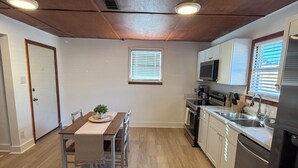 Una cocina moderna con suelo de madera, armarios blancos, electrodomésticos de acero inoxidable y un comedor con mesa y sillas.