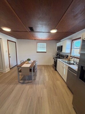 Eine moderne Küche mit Holzböden, weißen Schränken, Edelstahlgeräten und einem Essbereich mit Tisch und Stühlen.