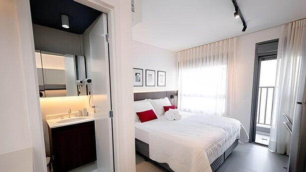 Une chambre d’hôtel avec un lit, une salle de bain avec un miroir et une fenêtre avec des rideaux.
