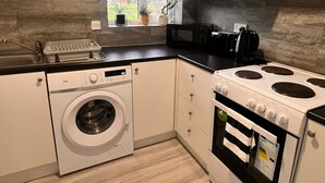 A compact kitchen with a washing machine, stove, and microwave. - Stylish 2-bedroom apartment in peaceful Manchester neighbourhood (Manchester)