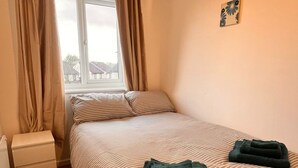 A bedroom with a bed, a nightstand, a window with curtains, and a wall decoration. - Stylish 2-bedroom apartment in peaceful Manchester neighbourhood (Manchester)