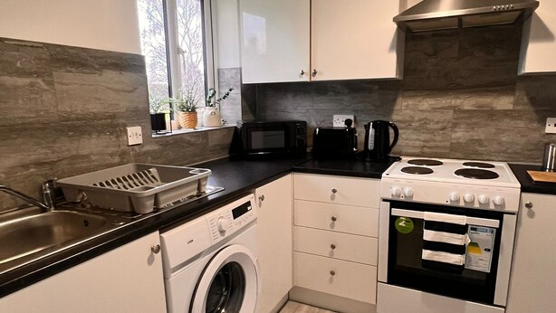 A compact kitchen with a washing machine, microwave, stove, and sink. - Stylish 2-bedroom apartment in peaceful Manchester neighbourhood (Manchester)