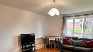 A living room with a TV, a sofa, a dining table, and a window with a view of buildings. - Stylish 2-bedroom apartment in peaceful Manchester neighbourhood (Manchester)