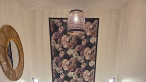 A bedroom with a large bed, two bedside tables with lamps, a decorative wall hanging, and a hanging light fixture.