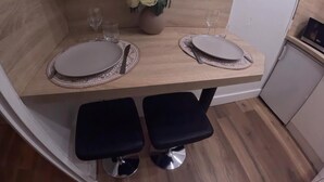 A compact dining area with two round tables, each with a matching placemat and a single wine glass. A vase with white flowers is centered on the table.