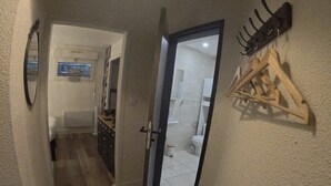 A narrow hallway with a wooden floor, a door leading to a bathroom, and a coat rack with hangers.