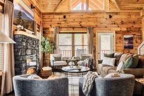 L’intérieur chaleureux d’un chalet en bois, avec une cheminée en pierre, des sièges confortables et une grande fenêtre donnant sur le paysage extérieur.
