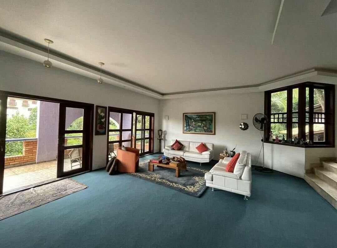 A spacious living room with a blue carpet, white sofas with red cushions, a coffee table, and a painting on the wall.