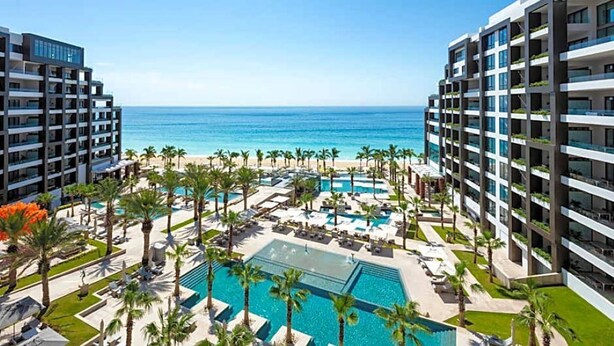 Un resort con varias piscinas, palmeras y vistas a la playa.