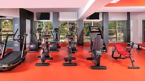 Un gimnasio moderno con máquinas de cardio, zonas de pesas y suelo rojo.