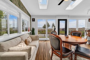 A modern interior with a dining area, sofa, and large windows offering a view of the outdoors. -  Oceanfront Seaglass Estate  Near Acadia National Park, with Hot Tub and Views! (Gouldsboro)