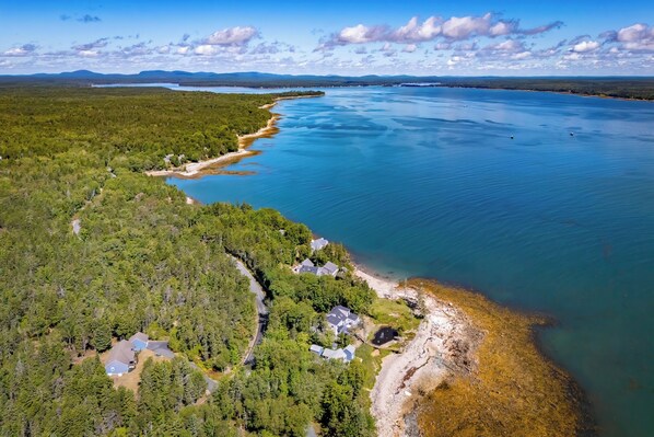 Vista aérea de una propiedad costera con un bosque denso, una playa y un mar azul cristalino.