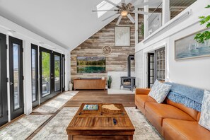 A modern living room with a fireplace, wooden flooring, a sofa, and a coffee table. -  Oceanfront Seaglass Estate  Near Acadia National Park, with Hot Tub and Views! (Gouldsboro)