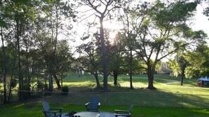 A circular outdoor seating area with Adirondack chairs and a fire pit, surrounded by a stone border, set in a grassy park with trees and a distant building. - Citrus Springs Golf & Country Club house / close to Crystal River. (Citrus Springs)