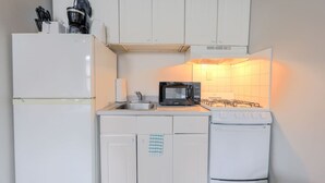A compact kitchen with white cabinets, a refrigerator, a microwave, a stove, and a sink. - Harmonious South End Studio (Boston)