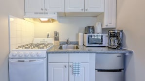 A compact kitchen with white cabinets, a gas stove, a microwave, a coffee maker, and a sink. - Blissful South End Studio (Boston)